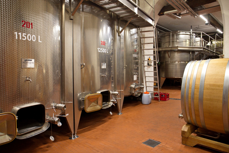 Cantina moderna con grandi serbatoi in acciaio inox numerati e botti in legno, parte dell'impianto di vinificazione dell'Abbazia Muri Gries